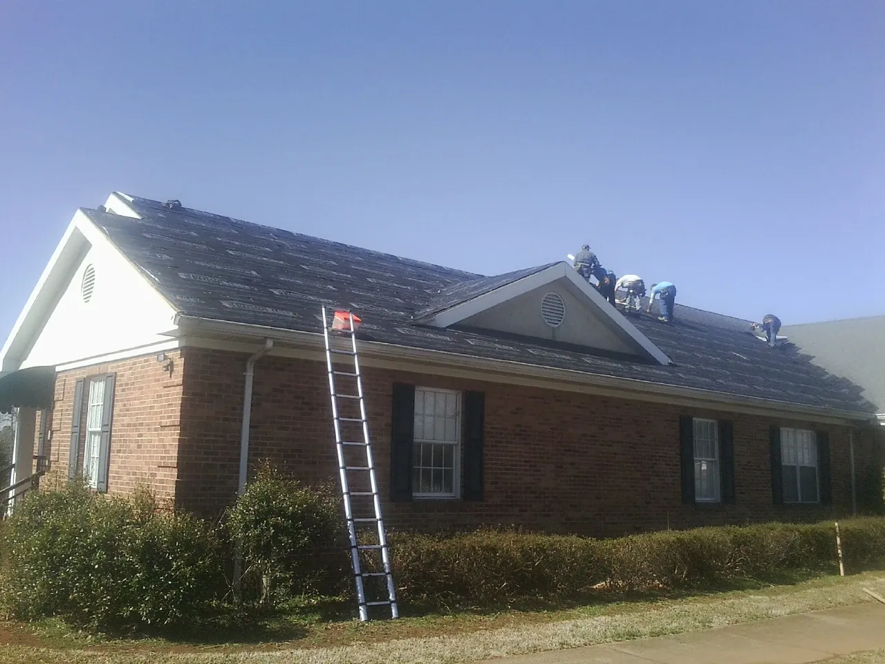 Crew tearing shingles off a brick ranch roof with a ladder set — Emergency Roof Repair work by our crew in Selma